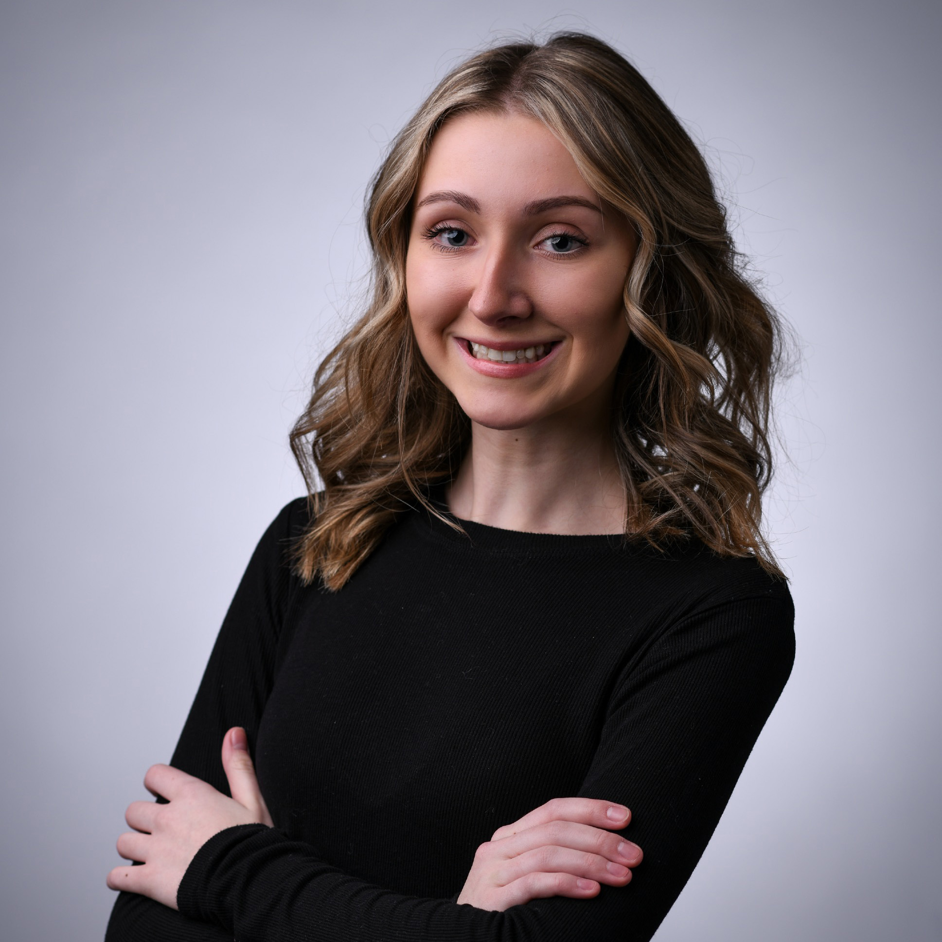 Madelyn Adamczyk smiles at the camera with crossed arms on a white background.
