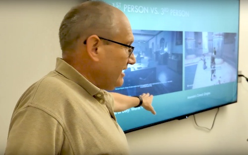 Professor gestures toward a screen displaying historical scenes during a classroom presentation.