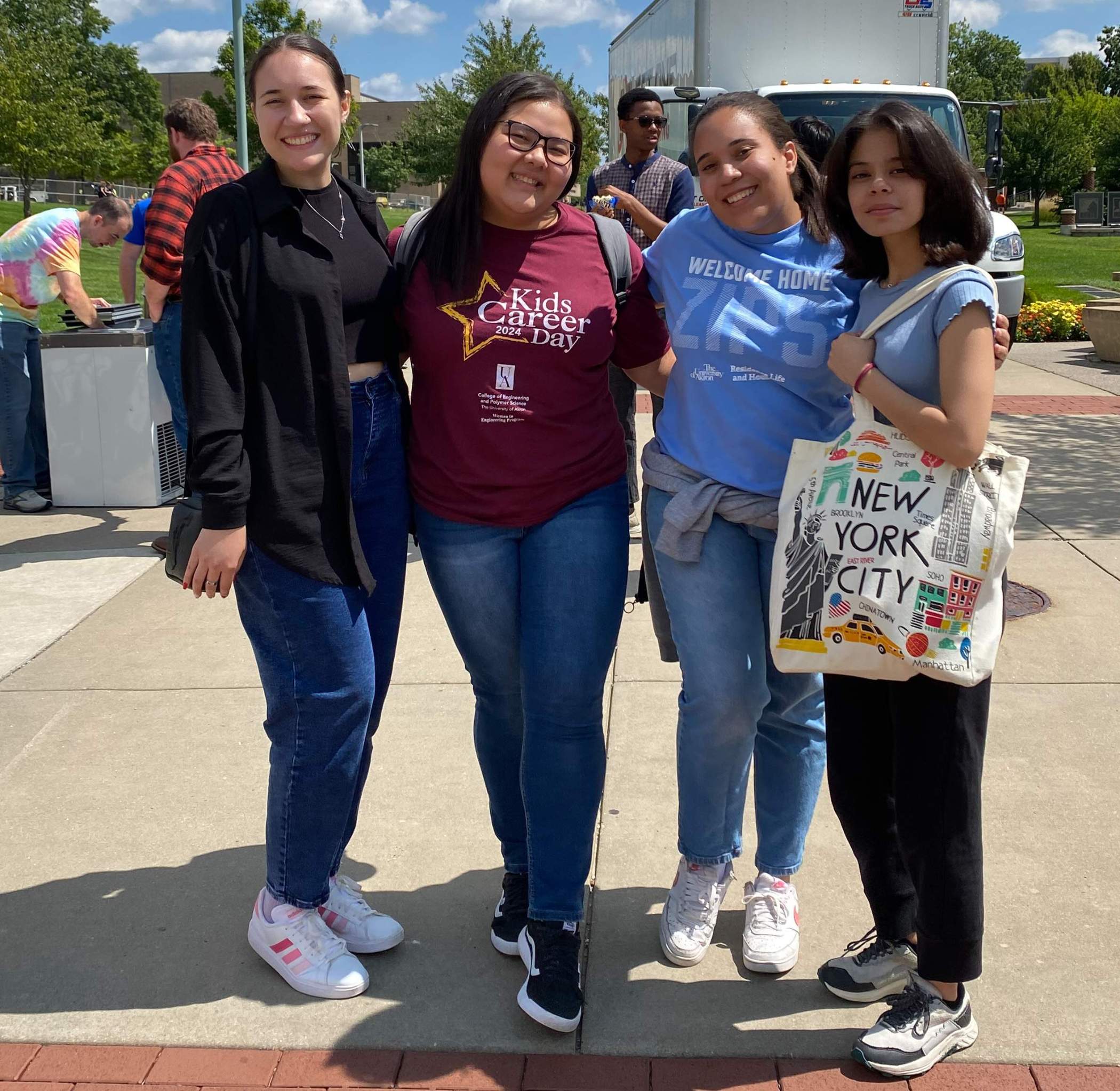 Photo of 4 students smiling as they stand together on Coleman Common at UA on a sunny day