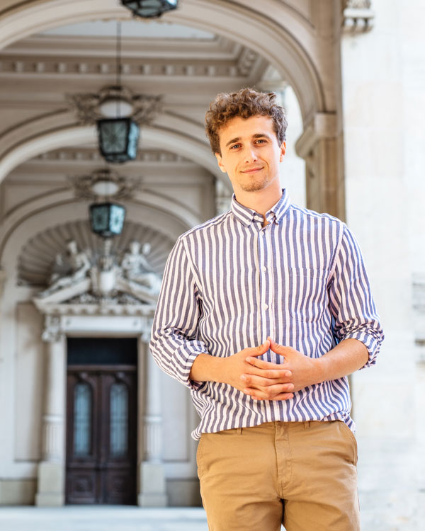 Student standing beneath an arched walkway in front of a historic building entrance.