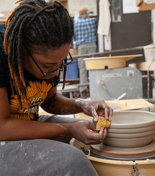 Ceramics student shapes a clay vessel on a pottery wheel.