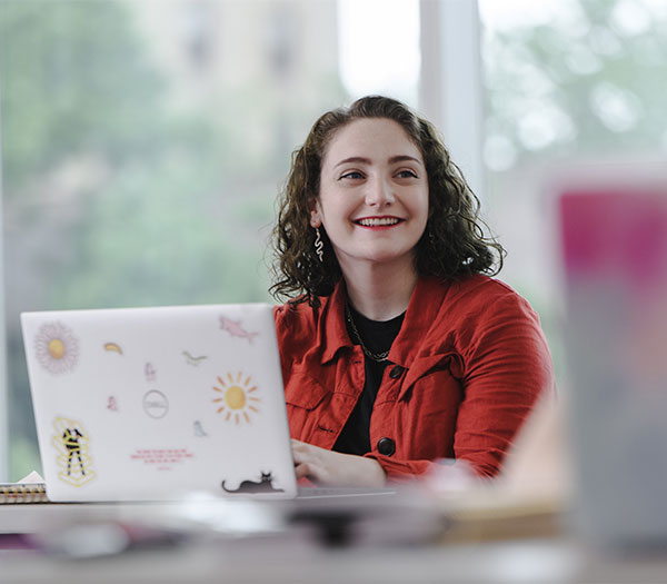 University of Akron student smiles while working on a laptop during a classroom discussion.