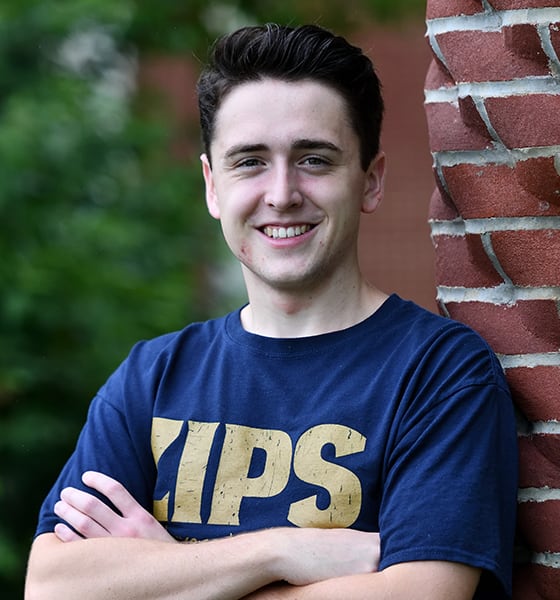 Max Pastoria leaning against a brick wall with his arms crossed, smiling