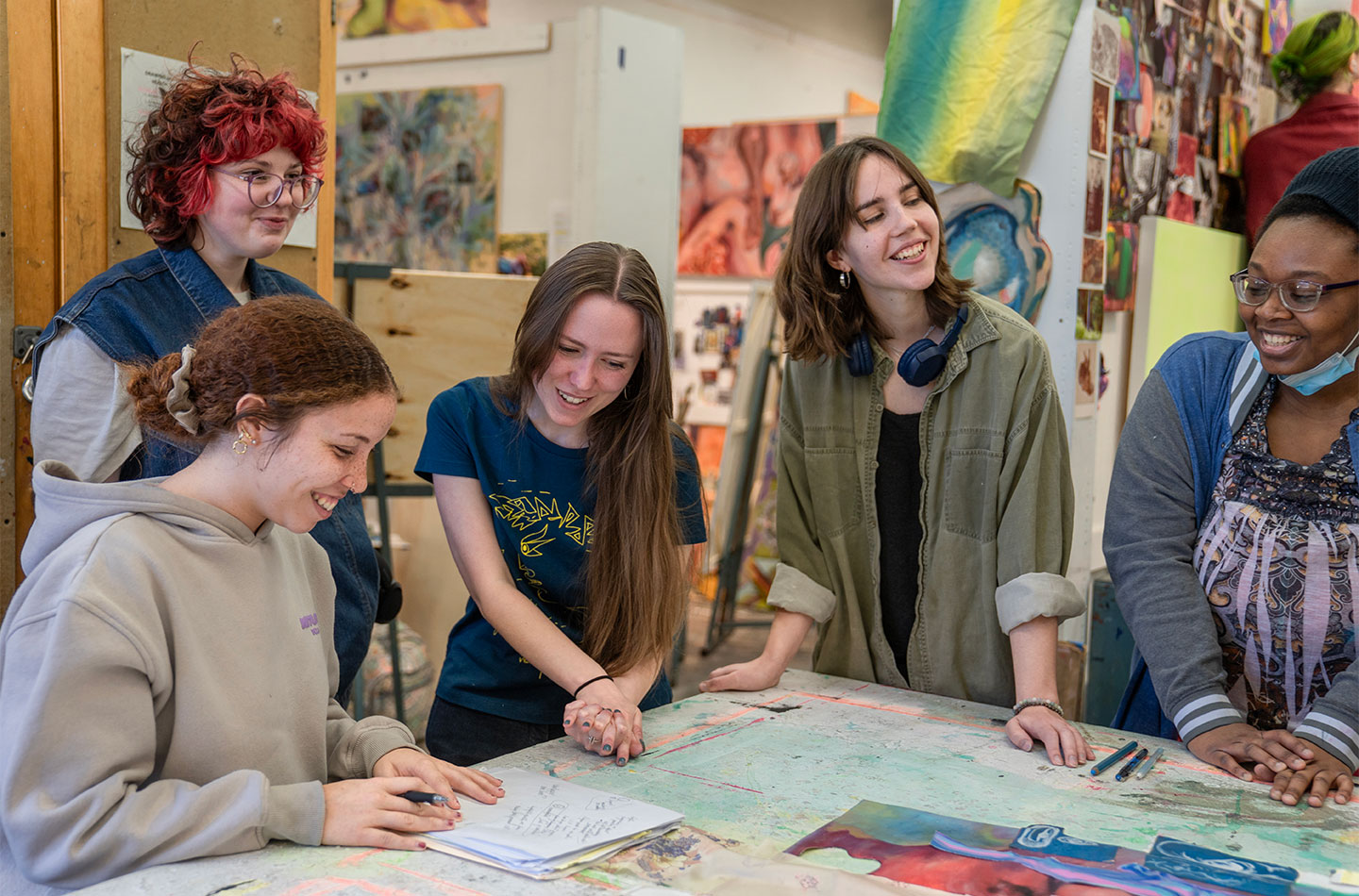Fine arts students collaborate around a studio table, reviewing sketches and artwork together.