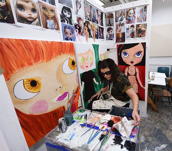 Painting student works in an individual studio surrounded by colorful paintings and reference images.
