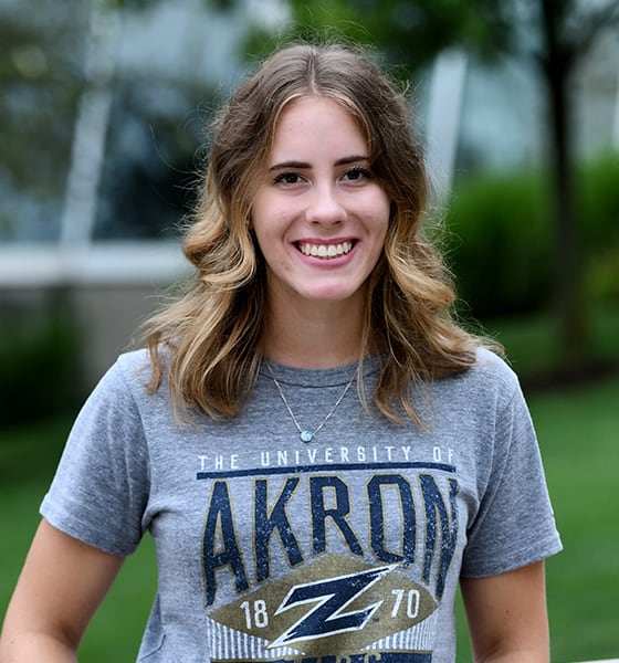 Ellie Riekert Standing against a brick wall while smiling
