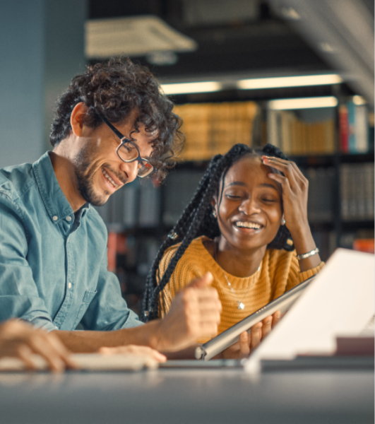 Caucasian man and African-American woman sitting in library working together and laughing