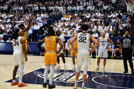 A basketball player in a yellow uniform shoots a free throw while players from both teams line up along the lane. The court is crowded with spectators in a large arena.