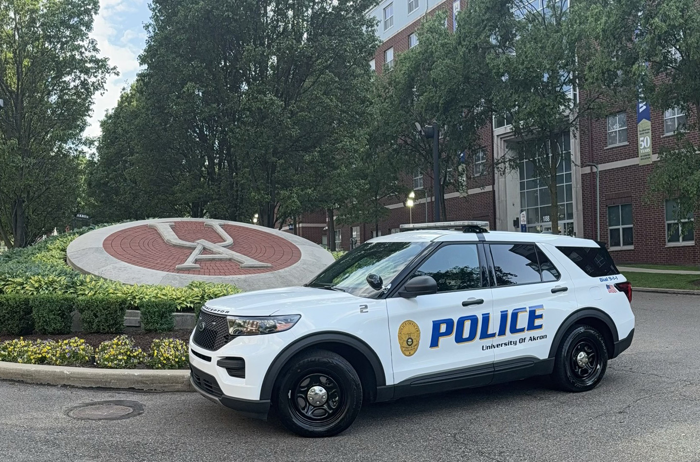 A University of Akron police cruiiser parked in front of the logo for UA at one of the entrances to the campus.