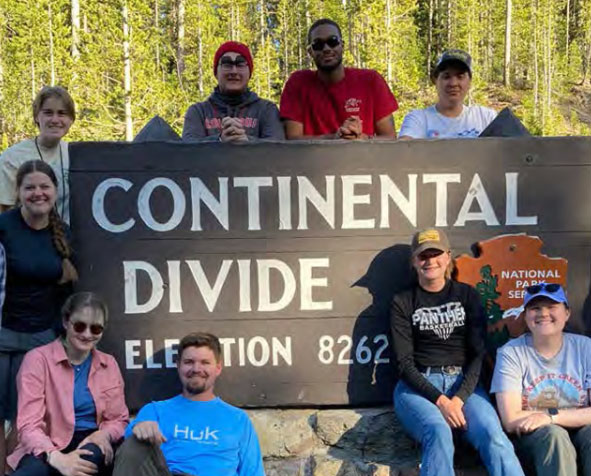 Group of University of Akron students posing beside a Continental Divide elevation sign during a field trip in a national park.