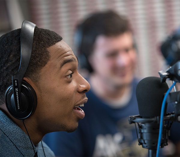 University of Akron student speaks into a microphone while hosting a WZIP radio broadcast in a campus studio.