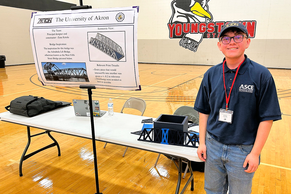 Zane Ketola stands with his bridge and poster for the 3D Printed Bridge competition.