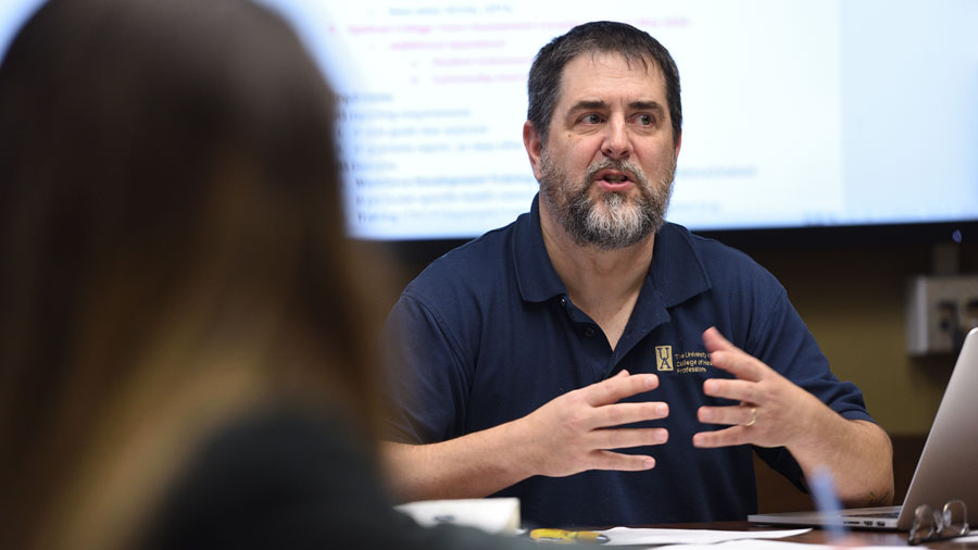 Man with facial hair in blue top speaking with hands.